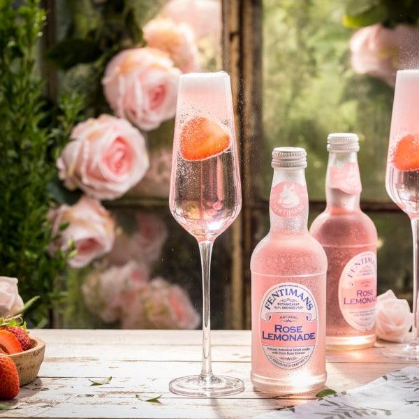 Fentimans Rose Lemonade bottles with glass of pink sparkling drink and strawberries, roses in background