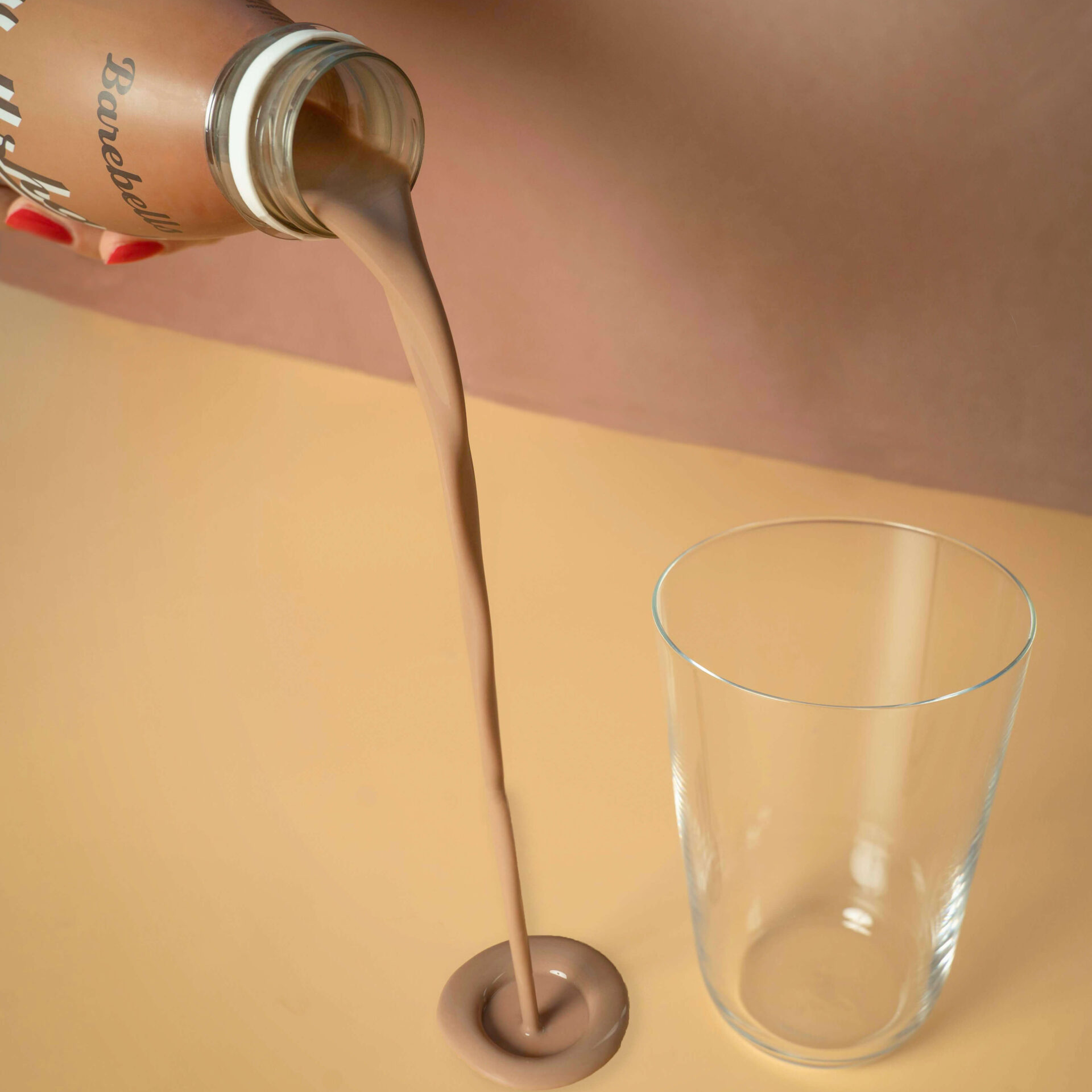Glass bottle being poured into a clear glass on a beige surface